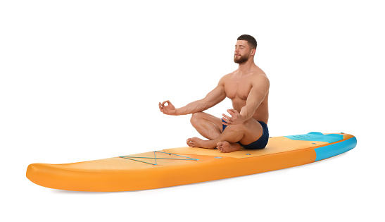 Handsome man practicing yoga on orange SUP board against white background
