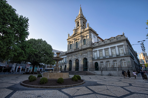 Street view of Church of the Santssima Trindade (Igreja da Santissima Trindade) in the morning, Porto, Portugal. A fountain and people can be seen walking by.