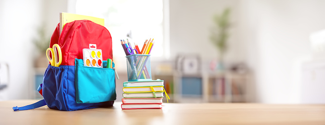 Colourful backpack with stationery standing on the table indoors. Concept of back to school.
