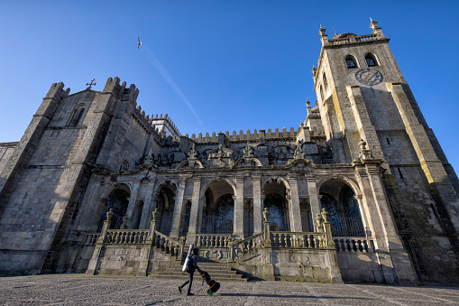 Exterior view of Porto Cathedral in the morning, Porto, Portugal. A woman with violin and pushing cart walking by.
