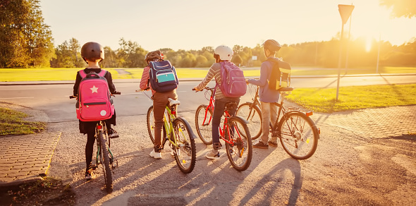 Boys and girl riding by bicycle to school together. Concept of back to school and friendship.