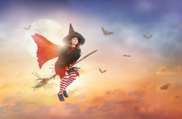 Little witch flying broom on Halloween night. Huge full moon and bats in the background. Kids trick or treat costume. Children have fun. Spooky and scary celebration. Kid dressed as evil ghost.