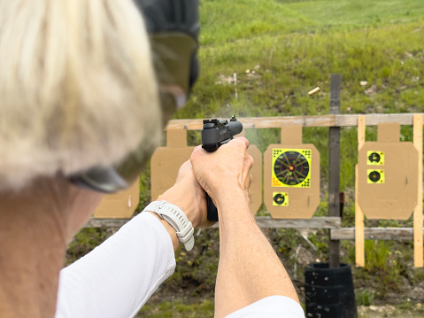 looking over the shoulder of a short hair, blond, caucasian, female shooting a 9 mm, black, handgun at a black and yellow target at the shooting range