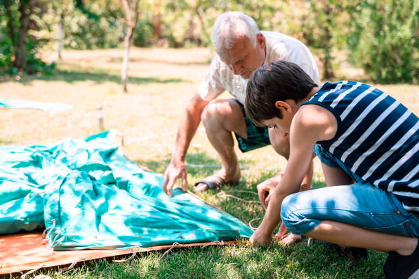 grandson and grandfather setting up tent tent. garden party. summer fun. child. - camping tent offspring 60s imagens e fotografias de stock