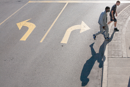 Two men crossing the street with their shadow on the pavement