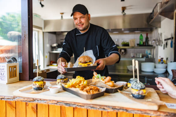 uśmiechnięty młody kaukaski szef kuchni niosący tacę z pysznym dużym burgerem mięsnym w małej restauracji typu fast-food - serving food restaurant chicken zdjęcia i obrazy z banku zdjęć