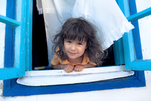 Smiling girl looking from a blue window with white curtains.