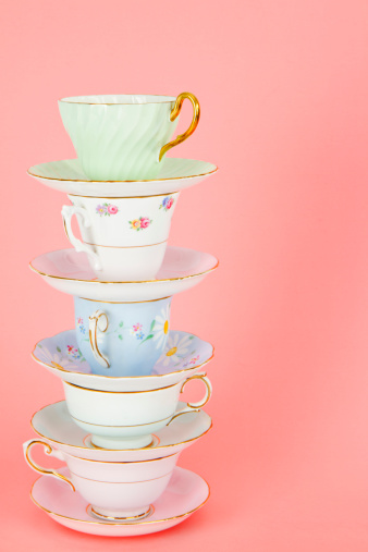 Pretty Antique Teacups On Pink. Four Pretty Old Fashioned Antique Teacups Stacked On Pink allows copy space on the right of the pile of cups. Each teacup is on it's matching saucer.  The teacups and saucer have 24carat gold on the brims.  
