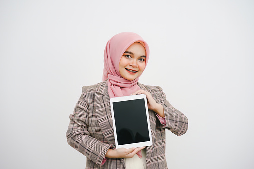 Portrait of beautiful young muslim businesswoman pink hijab indicates and show the digital tablet on white background. Concept usable for smartphone advertising