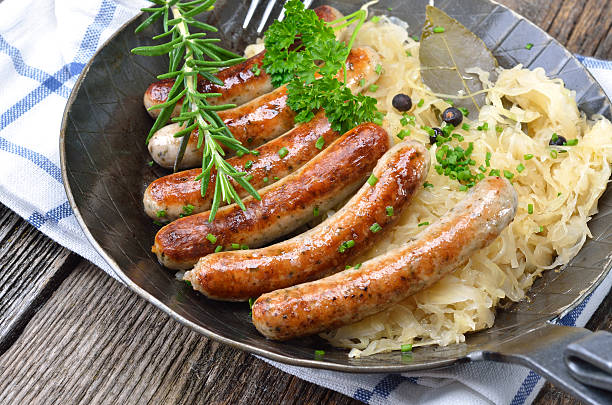 Sausages are served together with sauerkraut on a metal pan Bavarian fried sausages served with sauerkraut in a pan white cabbage stock pictures, royalty-free photos & images