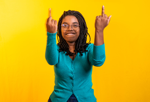 afrolatina woman using her two hands while holding her middle or middle finger up on a yellow background and blue blouse