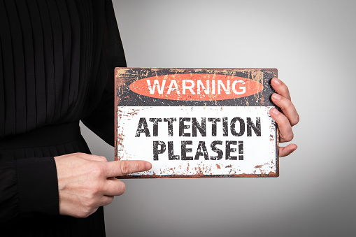 Attention please. Warning sign in a woman's hands on a light background.