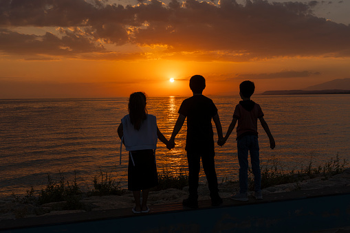 Mother and daughter holding hands, admiring beautiful sunset at Adriatic Sea beach. Silhouette of a family which trough shines Sunstar, Zaton, Croatia