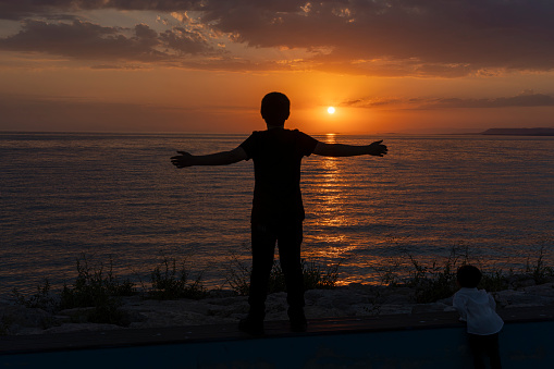 Boy standing on beach at sunset.