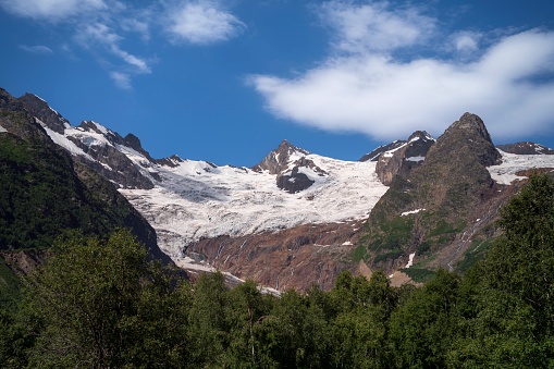 View of the Alibek glacier in the mountains of the North Caucasus on the territory of the Teberdinsky Nature Reserve on a sunny summer day, Dombay, Karachay-Cherkessia, Russia