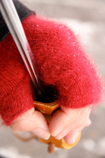 Vertical closeup photo of a woman’s hand wearing a possum fur and merino wool crimson red mitten, holding onto the wooden knob of an umbrella. Tiny raindrops are on the mitten. Soft focus snow background.