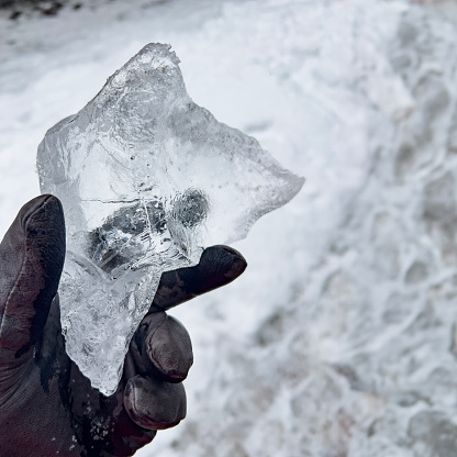 Hand in black leather gloves holding a piece of glacial ice. Macro view of ice in hand. Environment and climate change.