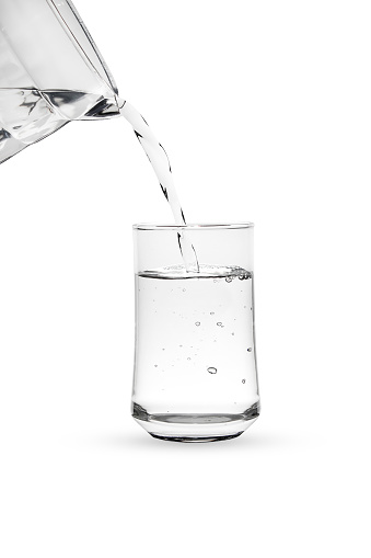 Pour water from glass jug into glass isolated on white background.