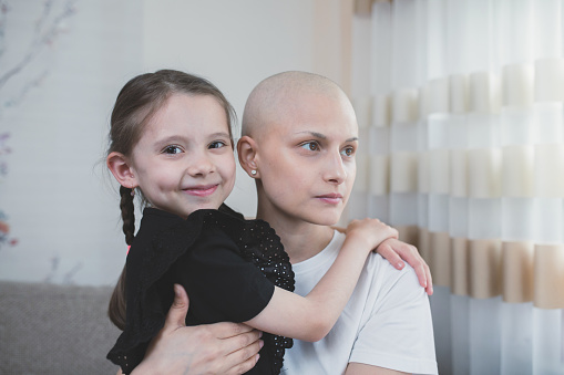 Small caring child embracing her ill bald mother after chemotherapy.