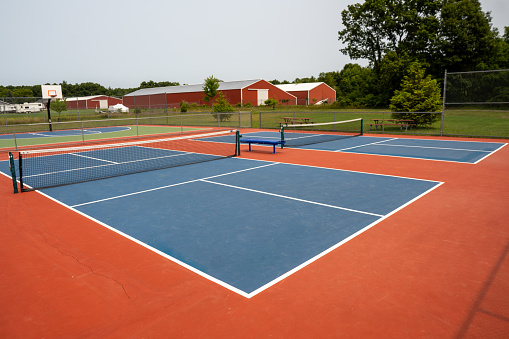 Recreational sport of pickleball court in Michigan, USA looking at an empty blue and orange clay colored court at a outdoor park.