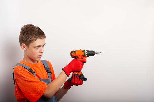 a teenage boy in a work uniform holds an electric drill