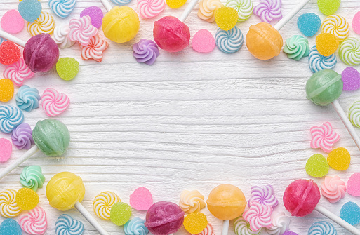 Colorful sweet lollipops and candies over white wooden background.