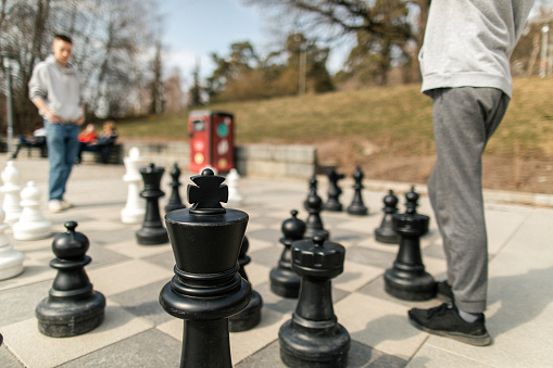 Two teenage boys are playing chess match in city park. They are playing street cheese with huge table board and figurines.