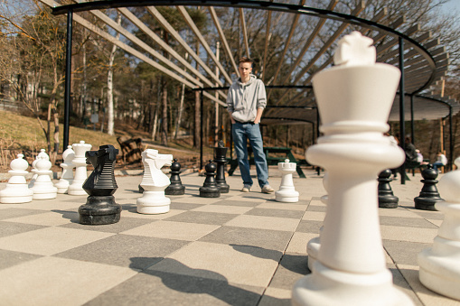 Two teenage boys are playing chess match in city park. They are playing street cheese with huge table board and figurines.