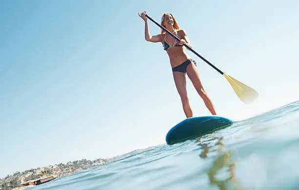 A beautiful woman out on the sea standing on her paddle board