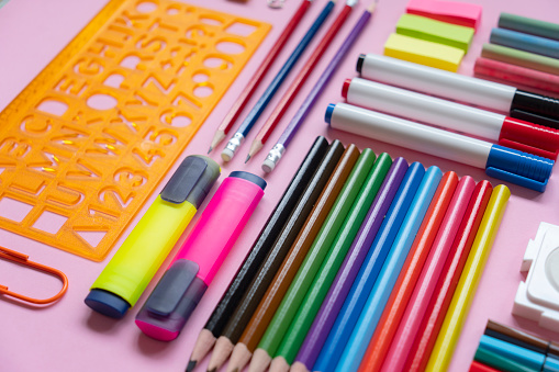 Office and school supplies arranged on pink background