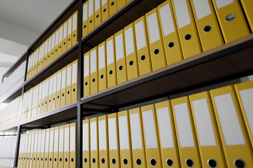 Yellow ring binders with files and documents put in long rows on shelves. Organized folder structure and archive on large rack in modern office