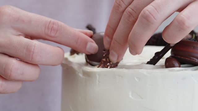 I am placing chocolate cookies on top of the white cream on the cake in slow motion.