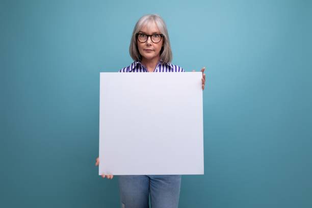 istock Successful grey-haired mature old lady shows blank billboard with mocap on bright studio background 1639803804