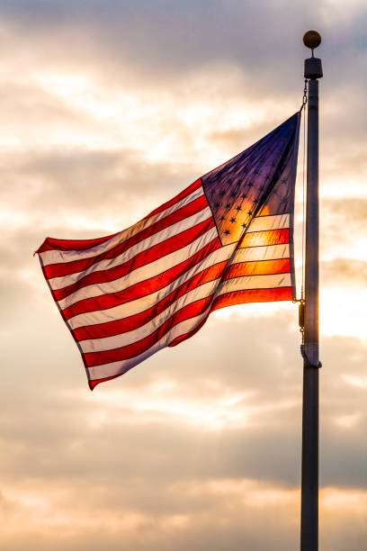 Stars and stripes flag backlit by sunlight, USA Stars and stripes American flag flying on a flag pole, backlit by sunlight against a sky flagpole stock pictures, royalty-free photos & images
