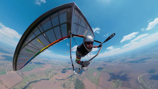 Hang glider pilot on the rainbow colored wing soars high in the sky