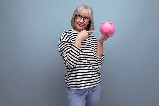 pleasant middle-aged woman 50 years old holding a piggy bank with savings on a bright background with copy space.