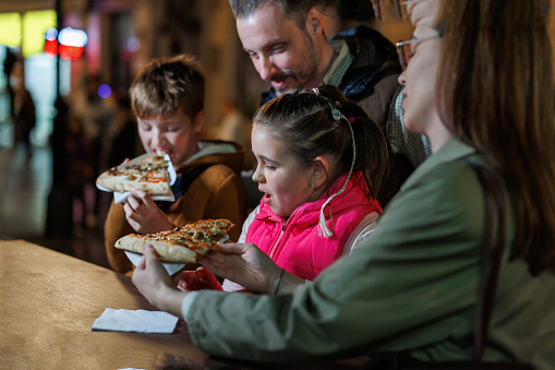 In the cozy ambiance of an outdoor setting, parents and siblings create treasured memories as they enjoy pizza together, the night sky above and the delicious flavors before them fostering a sense of unity and happiness