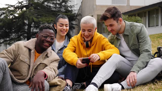 Group diverse students laugh and have fun watching cell phone outdoors. Cheerful young multiracial.