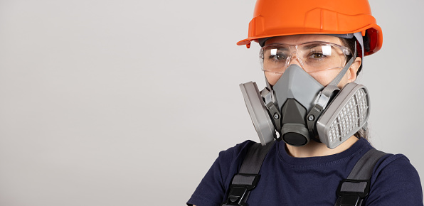 A woman wears a protective respirator with dust and gas filters on a white background