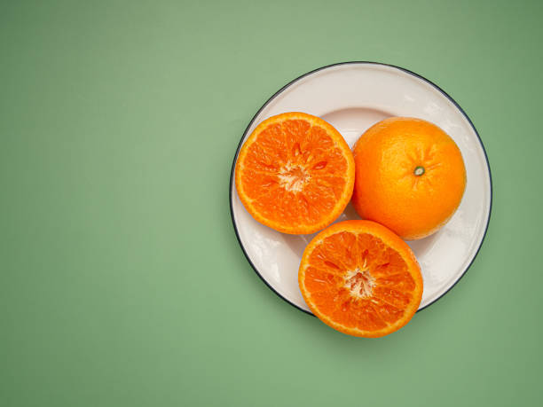 istock Top view of oranges cut half and whole on a white dish over a green background 1639965997