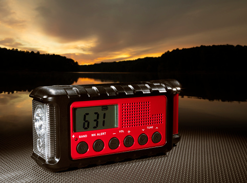 Sun glowing on the horizon over a lake's water with a red weather radio in the foreground.