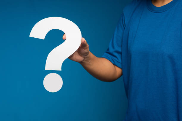 istock Close-up of hand holding a white question mark paper symbol while standing on a blue background 1639982926