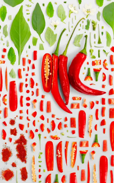 Abstract background made of Red Chili Pepper vegetable pieces, slices and leaves isolated on gray background.