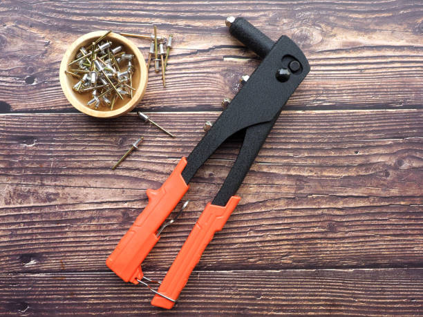 Hand Riveting tool with orange handle and bowl of blind rivets on wood table DIY, Hardware tools for repairing , Home work concept riveting stock pictures, royalty-free photos & images