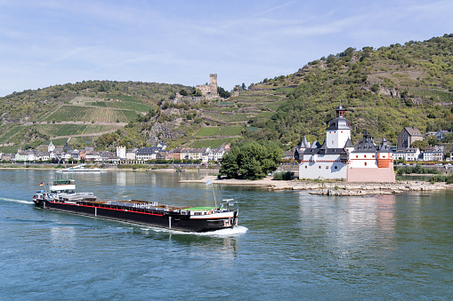 Inland general cargo vessel passing Pfalzgrafenstein Castle, a toll castle on the Falkenau island, in the River Rhine near Kaub, Germany.