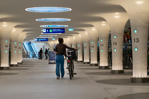 Amsterdam, Netherlands - July 17 2023: Back rear view of woman takes her bike from multistorey underground bike parking at the Central Station, Amsterdam, Holland