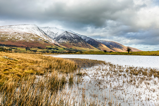 The shores of Tewet Tarn, with the snow capped hills of Blencathra, also known as Saddleback, in the distance, in the Lake District National Park near Keswick.