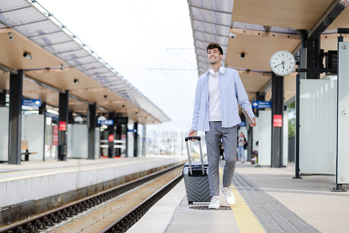 A young man, dressed in business-casual attire walking with his carry-on suitcase