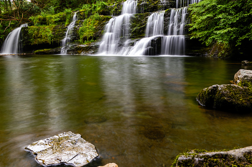 Cascading waterfall in a lush green forest (Sgwd y Pannwr, Wales)