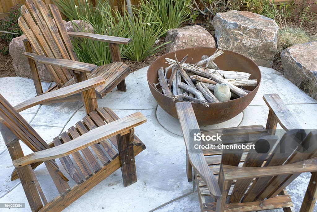 Residential Backyard Fire Pit A fire pit in a residential backyard with 3 wooden chairs and large rocks for seating. Fire Pit Stock Photo